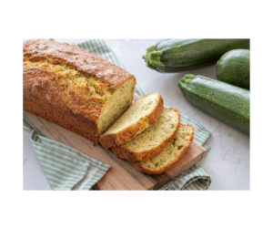 Freshly baked zucchini bread sliced on a wooden serving board with whole green zucchini displayed alongside the loaf.