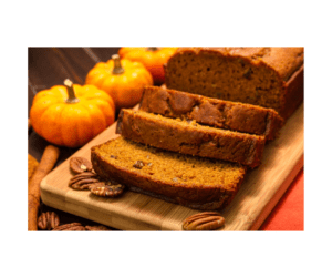 Freshly baked pumpkin pecan bread sliced on a wooden serving board with mini pumpkins, pecans, and warm fall spices.