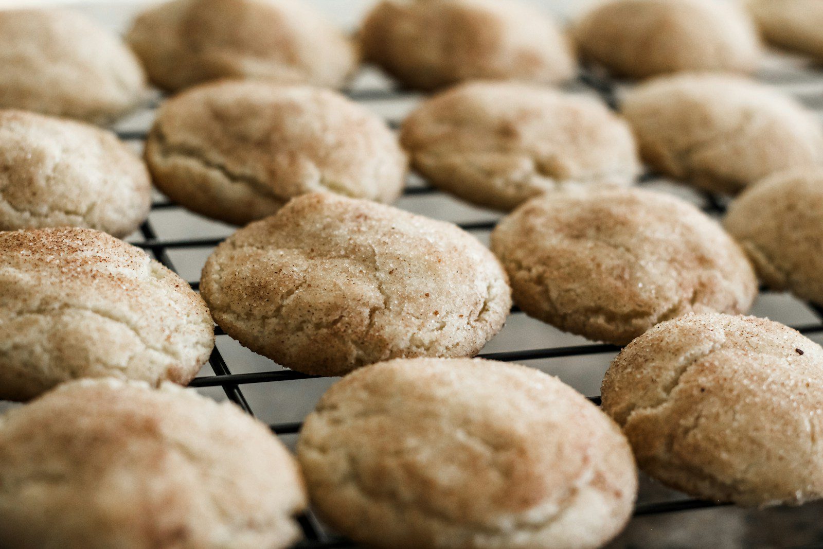 Freshly baked snickerdoodle cookies coated with cinnamon sugar cooling on a baking rack.