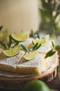Key lime dessert bars dusted with powdered sugar and garnished with fresh lime wedges.