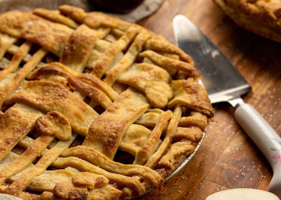 Freshly baked apple pie with a golden lattice crust surrounded by red apples and cinnamon sticks.