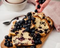 Sliced blueberry quick bread filled with fresh blueberries and served with additional berries.