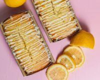Freshly baked lemon quick bread loaves topped with sweet lemon glaze and zest, surrounded by fresh lemon slices.