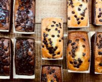 Assorted freshly baked quick bread loaves featuring chocolate and chocolate chip varieties arranged on a wooden table.