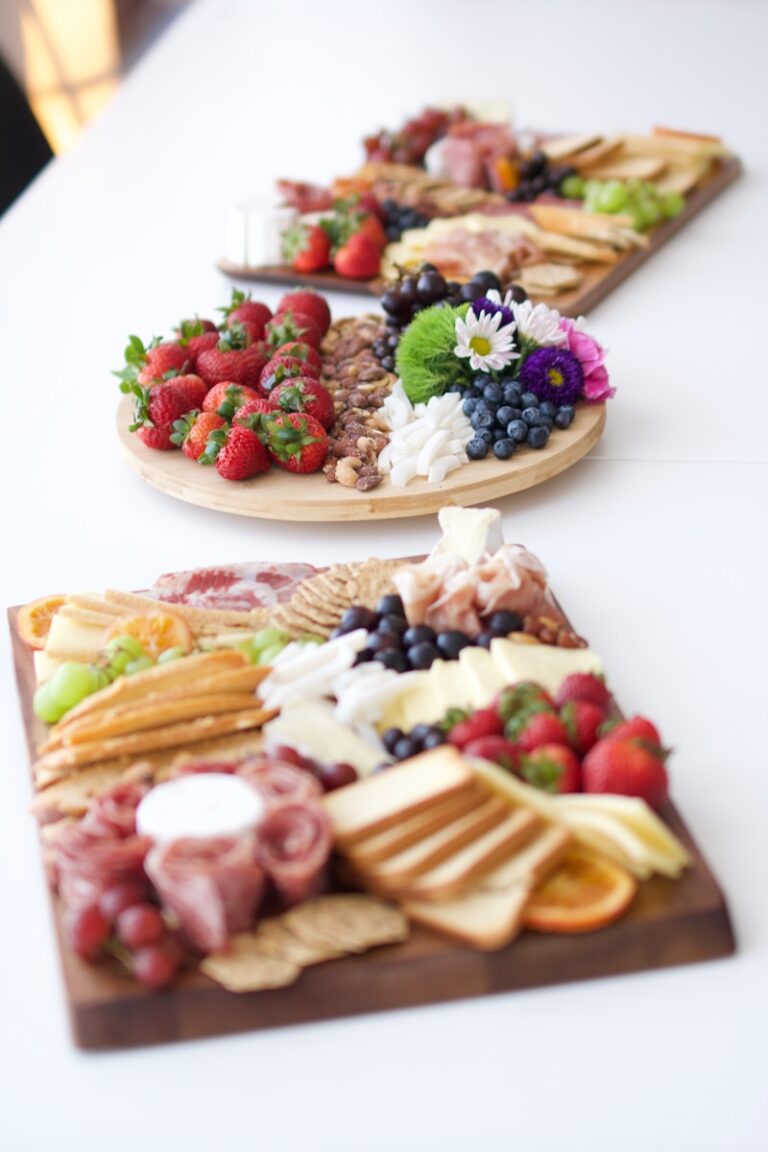 Elegant charcuterie boards arranged with strawberries, grapes, blueberries, cheeses, cured meats, crackers, nuts and fresh flowers.