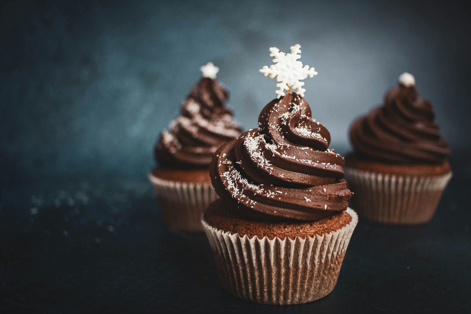 Chocolate cupcakes topped with rich chocolate frosting, white sprinkles, and decorative snowflake toppers.