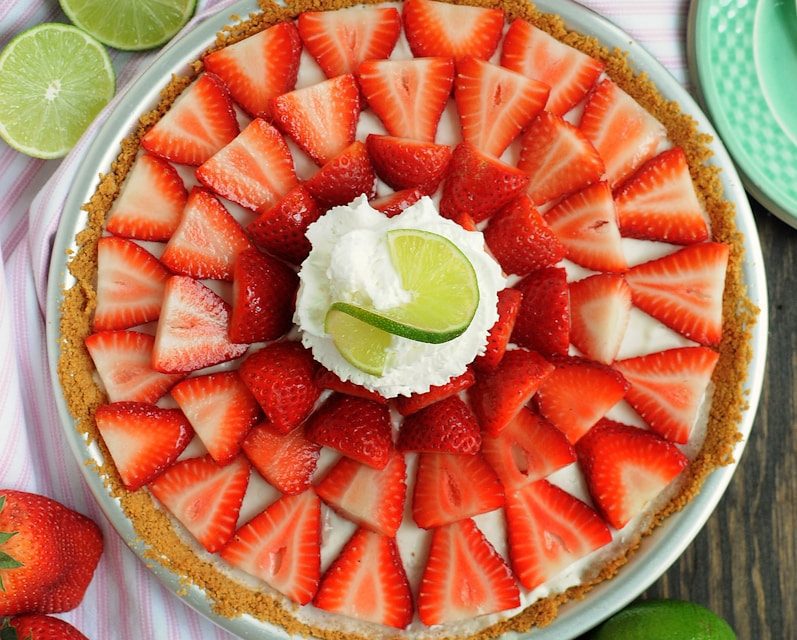 Creamy strawberry key lime pie with a graham cracker crust, topped with fresh strawberries, whipped cream, and lime garnish, perfect for catered dessert tables in Charleston, SC.