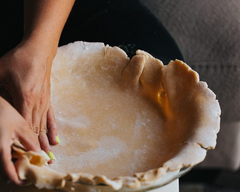 Hands pressing homemade pie crust into a glass pie dish, showcasing flaky pastry preparation for handcrafted pies and desserts in Charleston, SC.