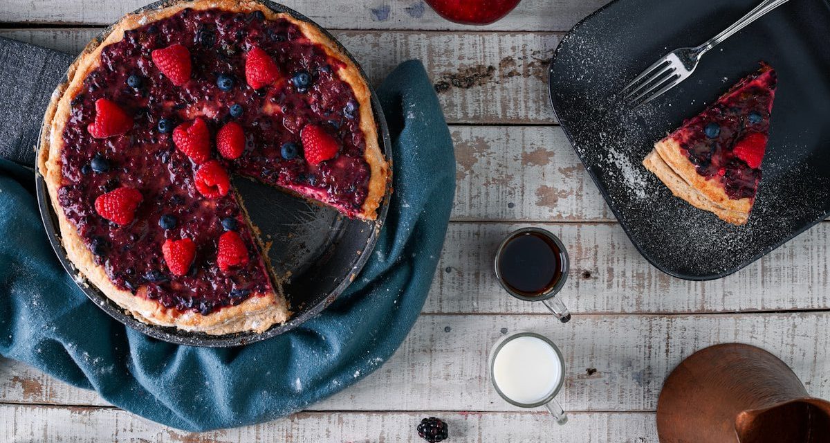Mixed berry pie with a flaky golden crust, topped with fresh raspberries and blueberries, served with a slice alongside coffee and milk for a homemade dessert in Charleston, SC.