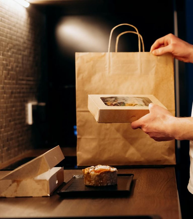 Prepared catered meal packaged in an eco-friendly takeout container and paper bag, representing convenient meal delivery and pickup catering services by Bites of Charleston in Charleston, SC.
