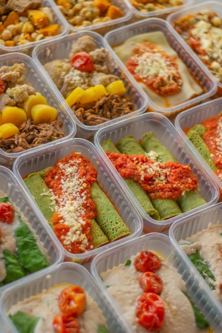 Assorted homemade meal prep containers featuring spinach crepes, lasagna, shredded beef, roasted vegetables, and protein-rich entrées ready for weekly meals.