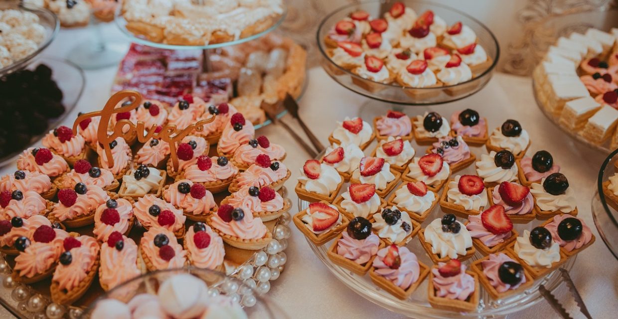 Elegant dessert buffet featuring mini fruit tarts, berry tartlets, cream-filled pastries, petit fours, and assorted bite-sized desserts beautifully displayed for a catered event.
