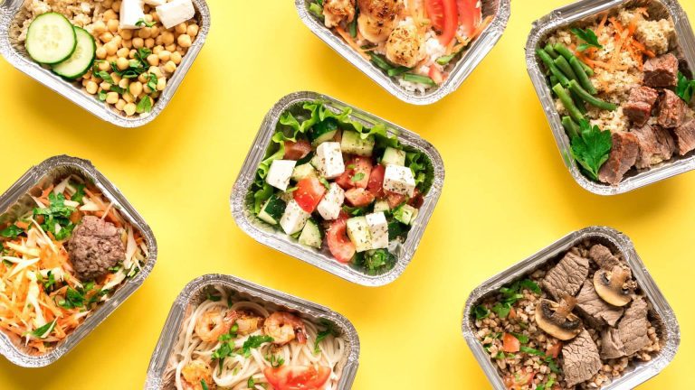 Assorted fresh meal prep containers featuring salads, grilled chicken, steak, shrimp, vegetables, grains, and healthy entrées ready for delivery.