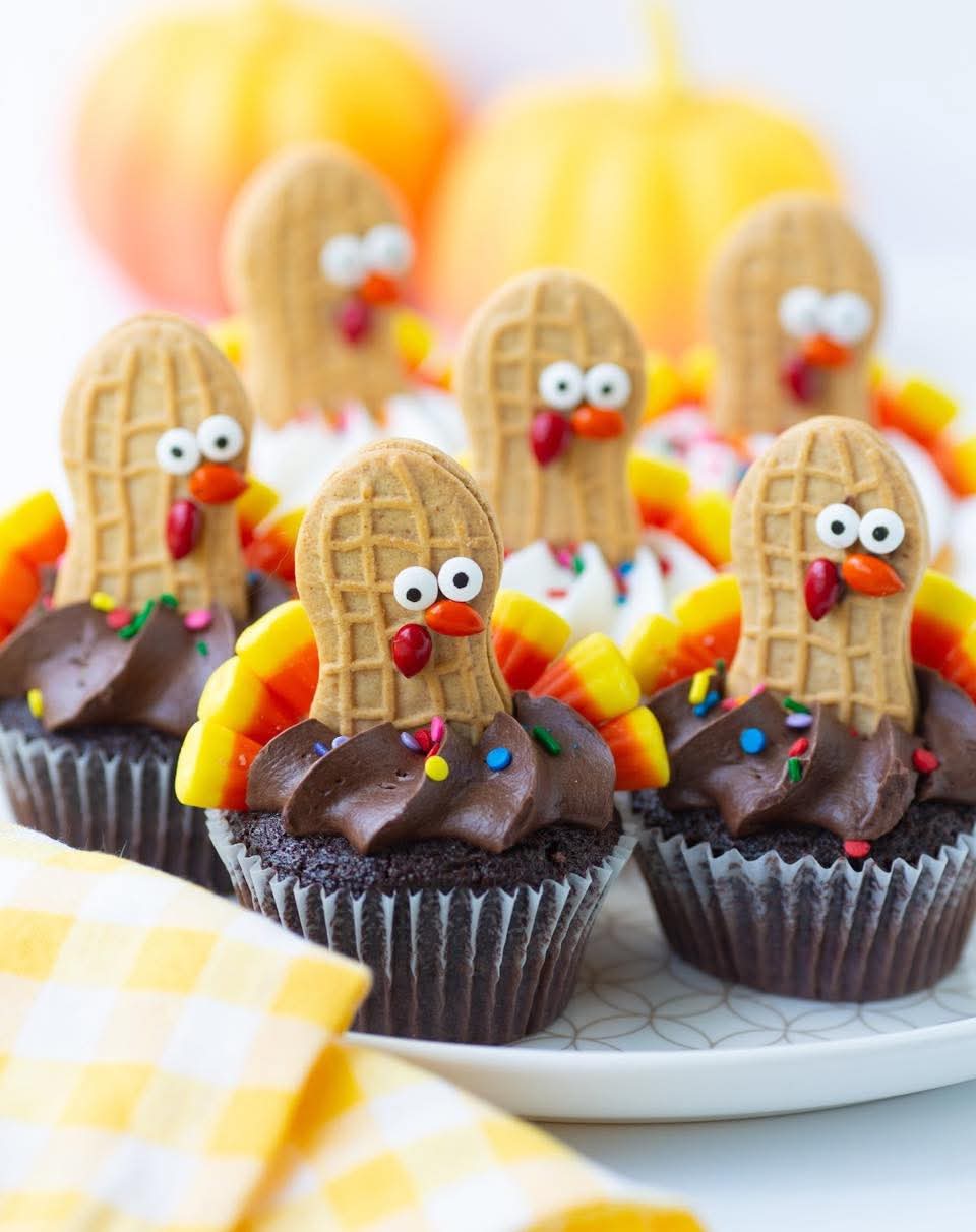Festive Thanksgiving turkey cupcakes decorated with peanut butter cookies, candy corn, frosting, and colorful sprinkles.