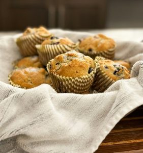 Freshly baked blueberry muffins dusted with powdered sugar, served warm in a cloth-lined basket for breakfast catering by Bites of Charleston in Charleston, SC.
