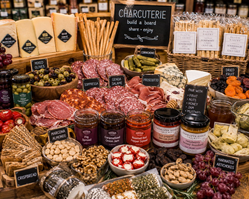 Charcuterie spread featuring artisan cheeses, cured meats, olives, nuts, dried fruit, crackers, jams, spreads, and gourmet accompaniments.